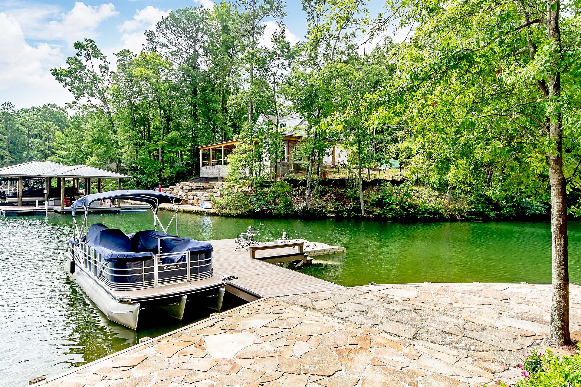 A residential lake dock with a moored pontoon boat and covered slip